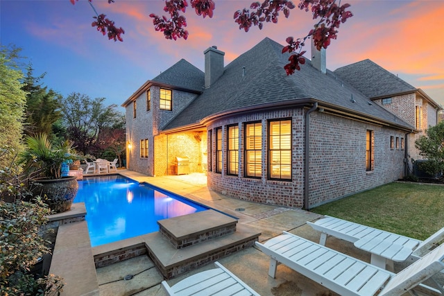 6405 Carmel Falls Ct, Mckinney, TX 75072 - back of property at dusk featuring a chimney, brick siding, a yard, a patio, and a shingled roof