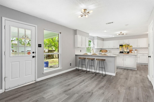 kitchen featuring light wood-style flooring, a peninsula, tasteful backsplash, and white cabinets
