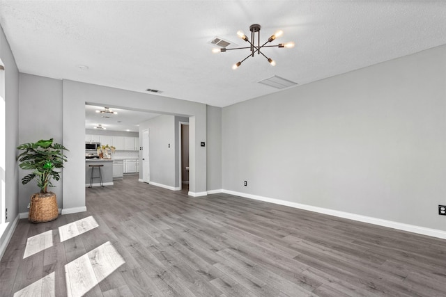 unfurnished living room with wood finished floors, an inviting chandelier, baseboards, and visible vents