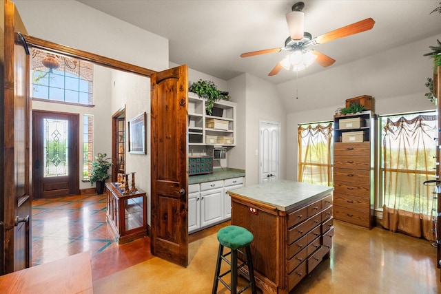 kitchen featuring a ceiling fan, a center island, open shelves, white cabinets, and lofted ceiling