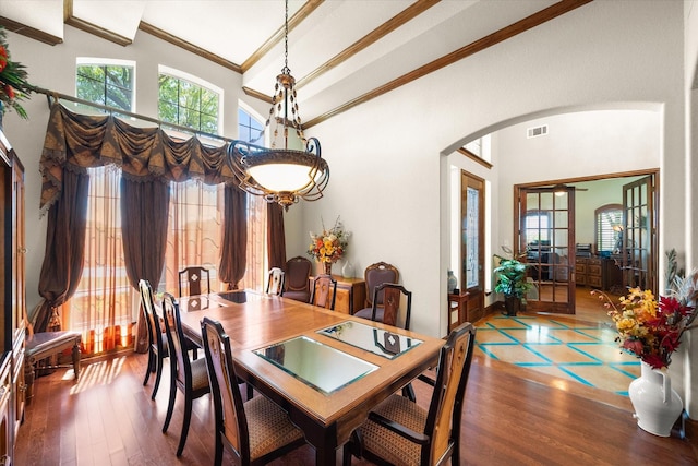 dining area with a towering ceiling, wood finished floors, visible vents, ornamental molding, and arched walkways