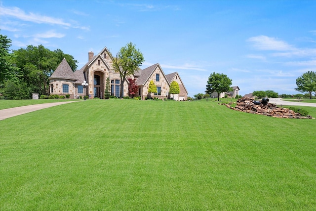 french country inspired facade with a chimney, stone siding, and a front yard