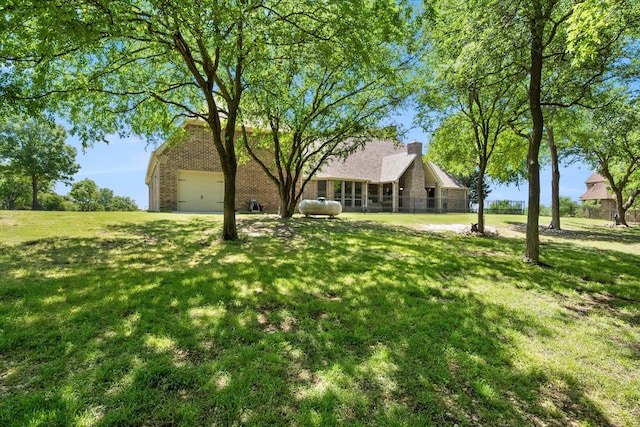 view of front of home with a chimney, brick siding, a front yard, and a garage