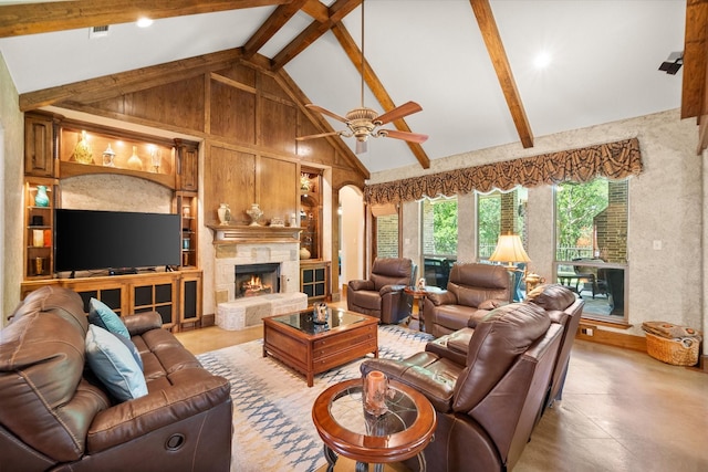 living area with a stone fireplace, a ceiling fan, beam ceiling, built in features, and high vaulted ceiling