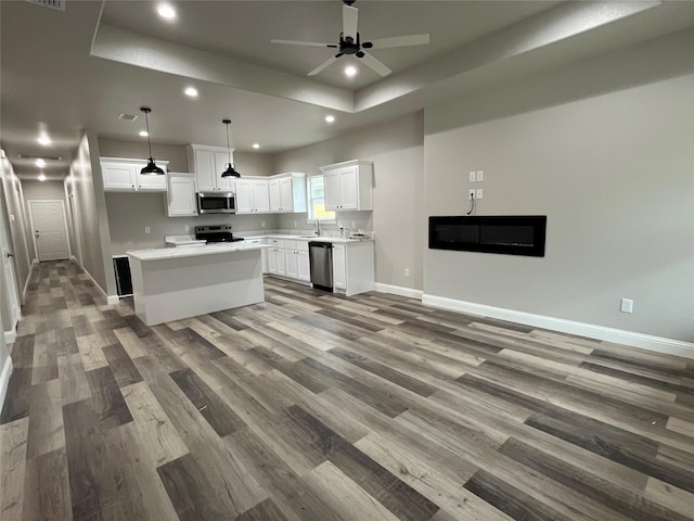 kitchen featuring a raised ceiling, baseboards, stainless steel appliances, recessed lighting, and white cabinetry