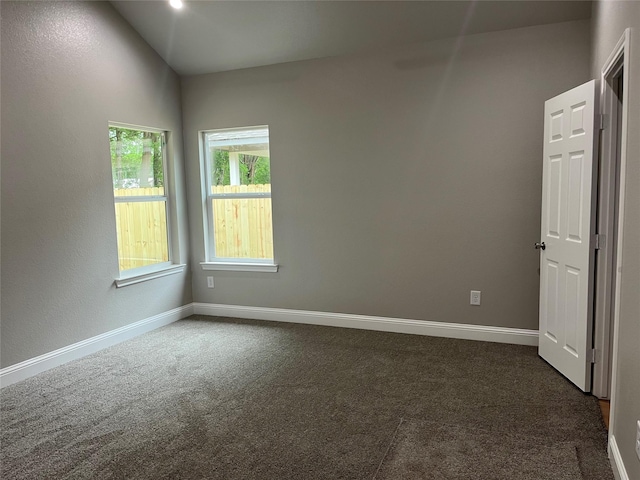 empty room featuring dark carpet, baseboards, and lofted ceiling