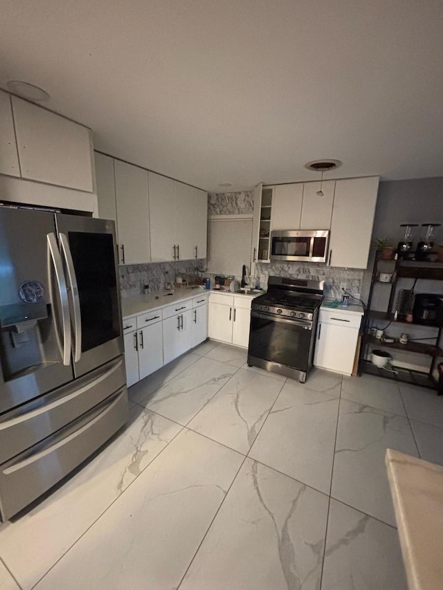 kitchen with tasteful backsplash, white cabinetry, marble finish floor, light countertops, and stainless steel appliances