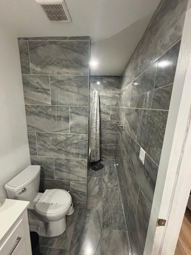 full bath with a tile shower, vanity, visible vents, and toilet
