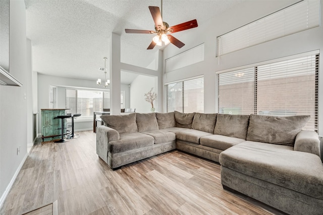 living room with a textured ceiling, baseboards, light wood finished floors, ceiling fan with notable chandelier, and a towering ceiling