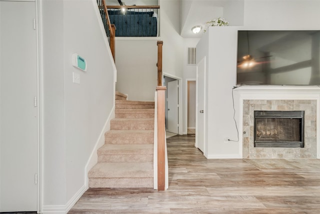 stairs with baseboards, a tile fireplace, visible vents, and wood finished floors