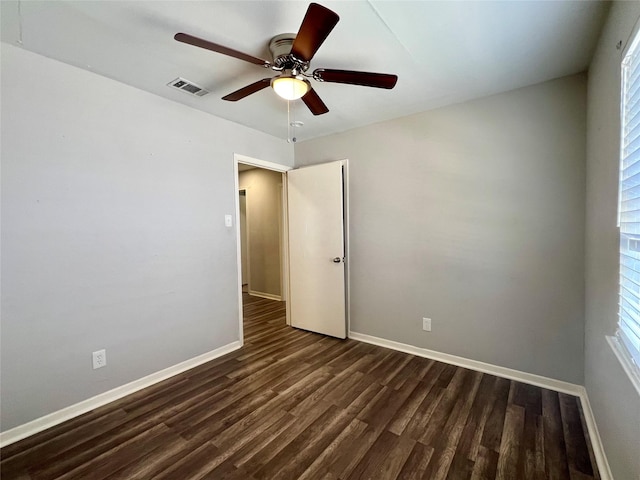 spare room with dark wood-type flooring, visible vents, baseboards, and a ceiling fan