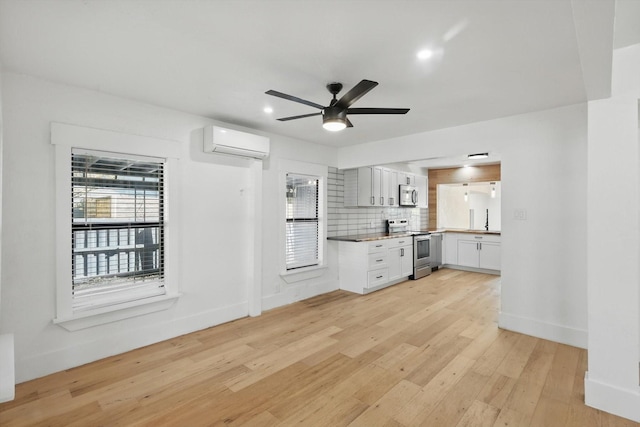 unfurnished living room featuring an AC wall unit, light wood-type flooring, ceiling fan, baseboards, and recessed lighting