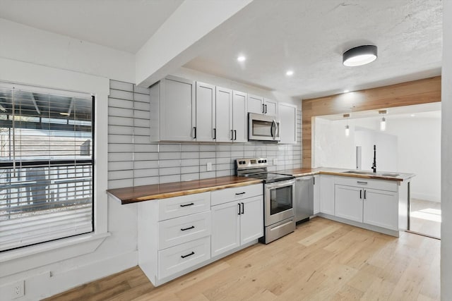 kitchen with stainless steel appliances, butcher block counters, a sink, a peninsula, and decorative backsplash