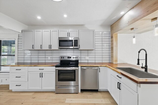 kitchen featuring stainless steel appliances, a sink, wood counters, decorative backsplash, and a peninsula