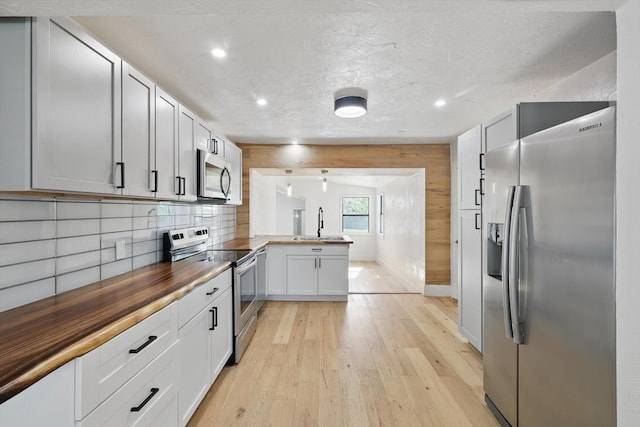 kitchen with appliances with stainless steel finishes, butcher block countertops, a peninsula, light wood finished floors, and recessed lighting