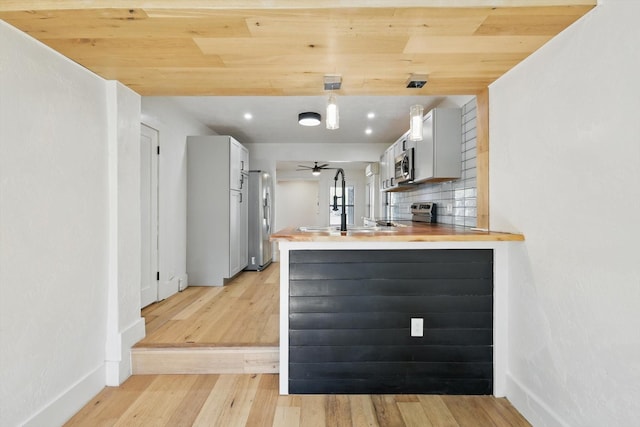 kitchen with stainless steel appliances, light wood-style flooring, a peninsula, baseboards, and backsplash