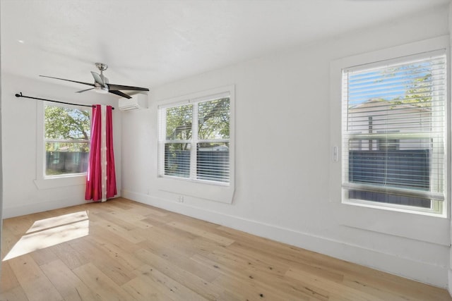 empty room with a wall mounted air conditioner, light wood-style floors, a ceiling fan, and baseboards