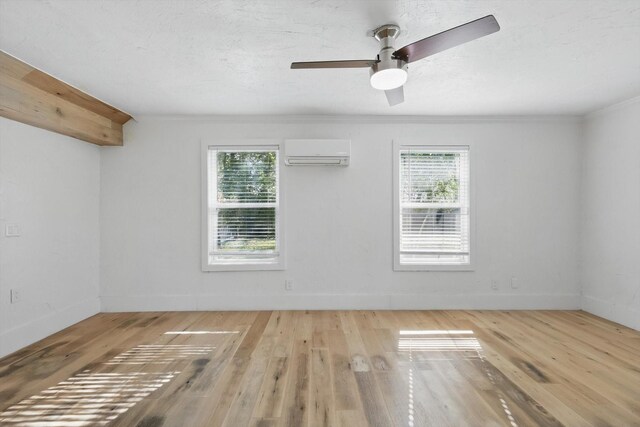unfurnished room with a wall mounted air conditioner, hardwood / wood-style flooring, plenty of natural light, ornamental molding, and baseboards