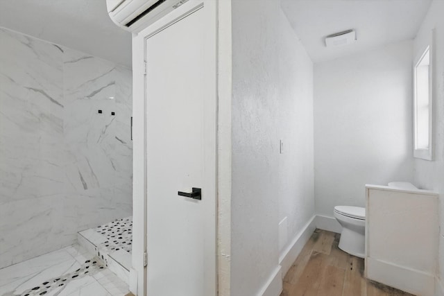 bathroom featuring a marble finish shower, a wall mounted air conditioner, toilet, wood finished floors, and baseboards