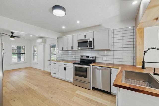 kitchen featuring wooden counters, appliances with stainless steel finishes, a sink, an AC wall unit, and a ceiling fan