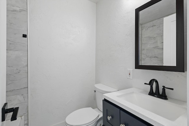 bathroom with toilet, vanity, and a textured wall