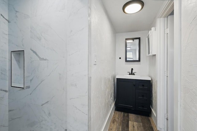 full bath featuring wood finished floors, vanity, a marble finish shower, and baseboards