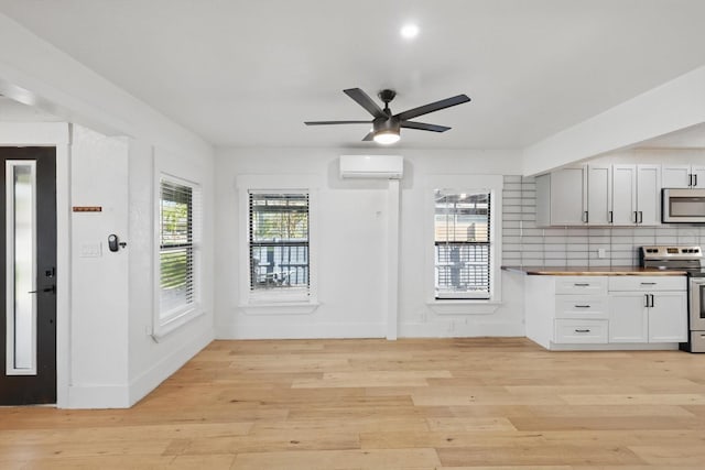 kitchen with appliances with stainless steel finishes, wood counters, a wall mounted air conditioner, light wood-style flooring, and ceiling fan