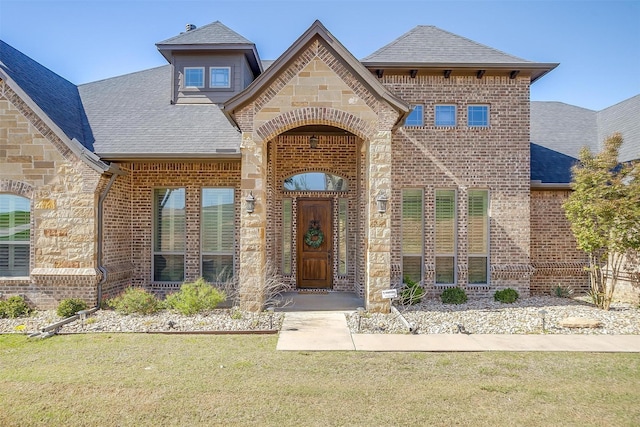 entrance to property with brick siding, a lawn, and roof with shingles