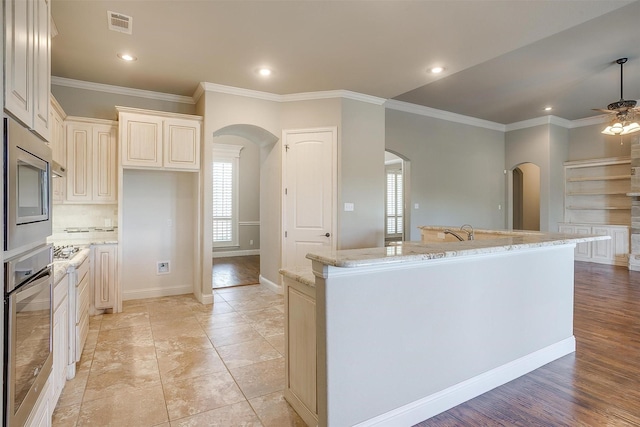 kitchen with arched walkways, ornamental molding, a ceiling fan, light stone countertops, and stainless steel appliances