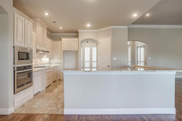 kitchen featuring arched walkways, appliances with stainless steel finishes, light stone counters, and visible vents