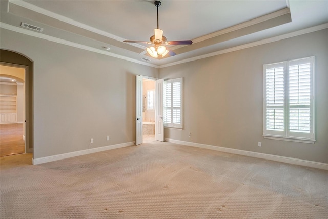 spare room with a wealth of natural light, a tray ceiling, arched walkways, visible vents, and light carpet
