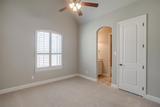 unfurnished bedroom featuring ensuite bathroom, baseboards, arched walkways, vaulted ceiling, and light colored carpet