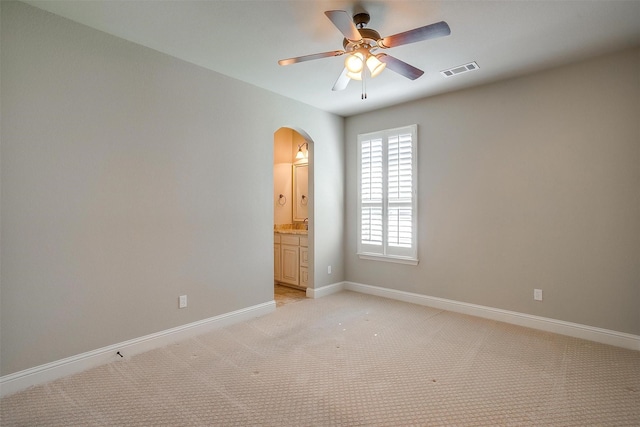 unfurnished room with baseboards, a ceiling fan, visible vents, arched walkways, and light colored carpet