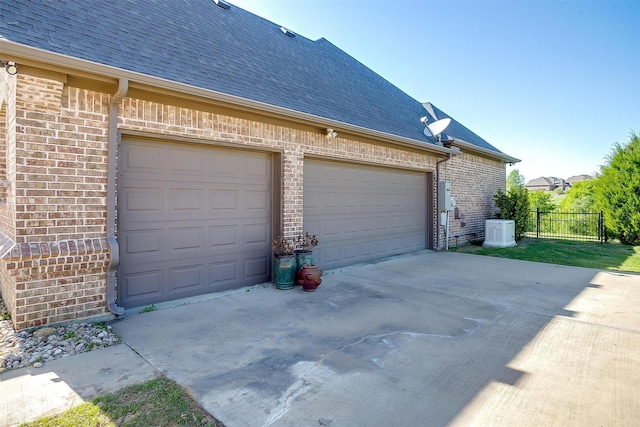 view of side of property with a shingled roof, a garage, fence, concrete driveway, and brick siding