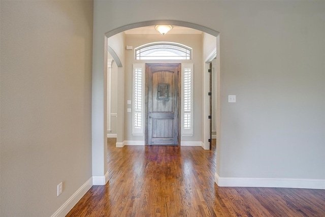 foyer entrance featuring arched walkways, a healthy amount of sunlight, wood finished floors, and baseboards