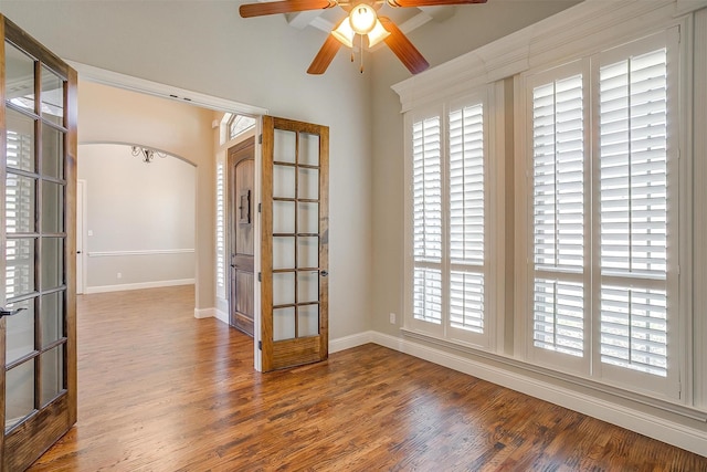 unfurnished room with baseboards, french doors, a ceiling fan, arched walkways, and wood finished floors