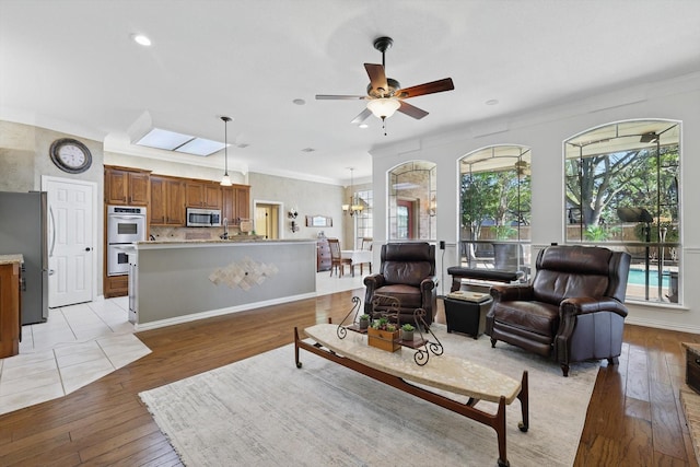 living area featuring ornamental molding, light wood finished floors, recessed lighting, and ceiling fan with notable chandelier