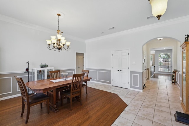 dining space featuring a decorative wall, arched walkways, ornamental molding, visible vents, and a chandelier