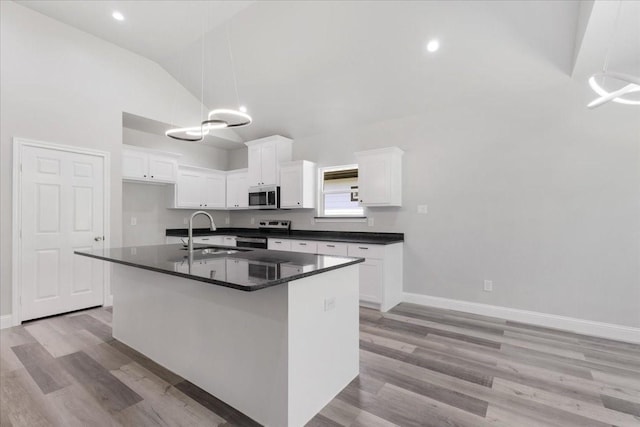 kitchen featuring dark countertops, white cabinets, lofted ceiling, stainless steel appliances, and a sink