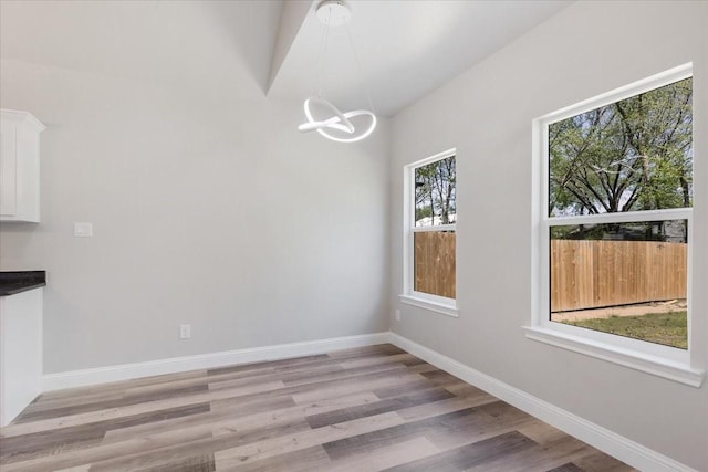 unfurnished dining area with baseboards, light wood-type flooring, and a chandelier