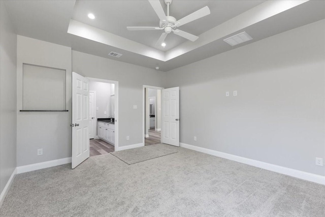 unfurnished bedroom featuring visible vents, baseboards, a raised ceiling, carpet floors, and recessed lighting