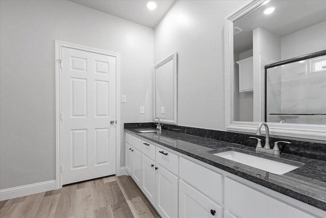 full bath with a shower with shower door, double vanity, a sink, and wood finished floors