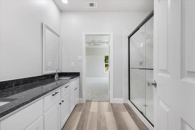 bathroom with visible vents, a sink, a shower stall, double vanity, and wood finished floors