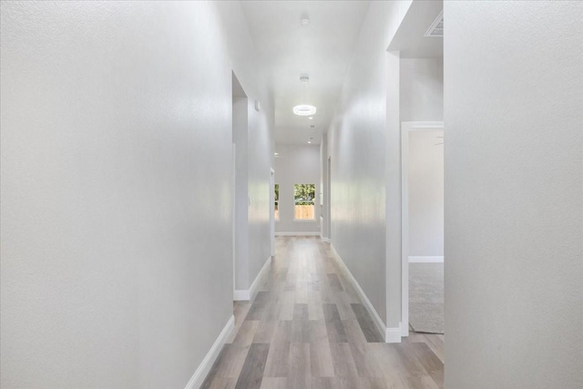 hallway with light wood-style flooring, baseboards, and visible vents