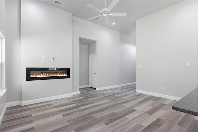 unfurnished living room with visible vents, baseboards, ceiling fan, wood finished floors, and a glass covered fireplace