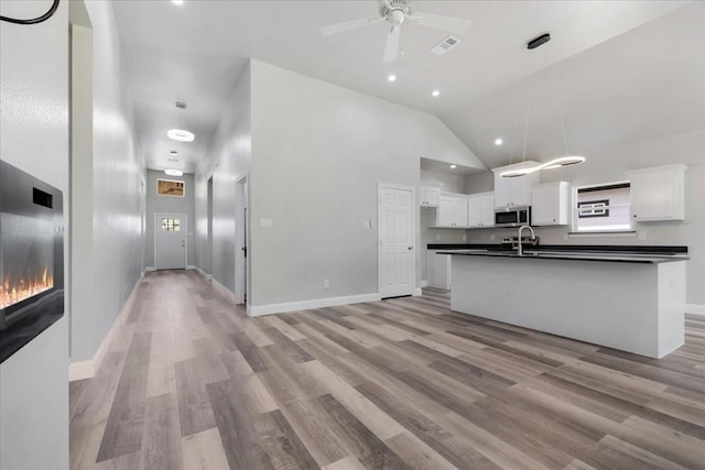 kitchen featuring a sink, ceiling fan, dark countertops, light wood-style floors, and stainless steel microwave