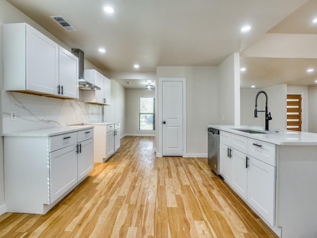 kitchen featuring wall chimney range hood, light countertops, visible vents, dishwasher, and a sink