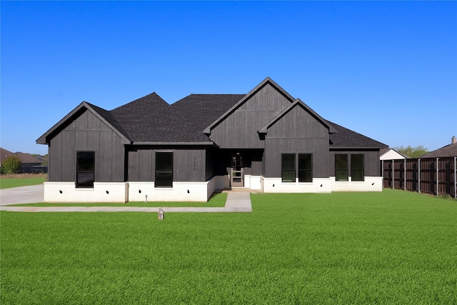 back of property featuring roof with shingles, fence, and a lawn