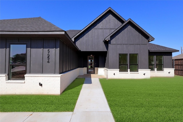 view of front of home featuring brick siding, roof with shingles, board and batten siding, and a front lawn
