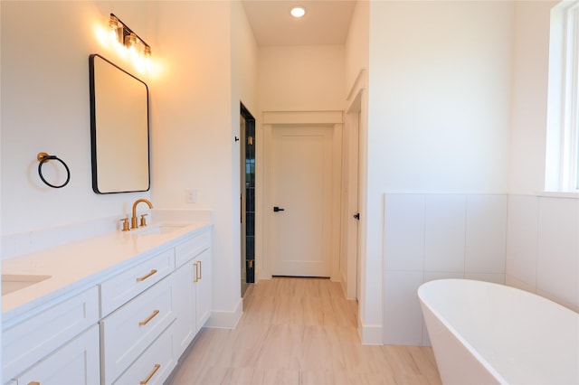 bathroom featuring a freestanding bath, recessed lighting, double vanity, and a sink